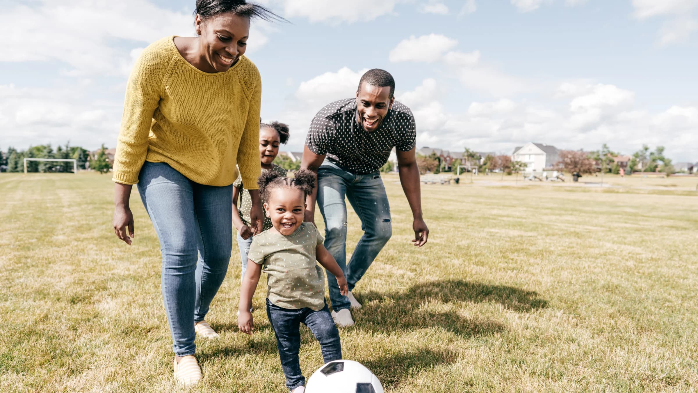 Family playing soccer together in a sunny park
